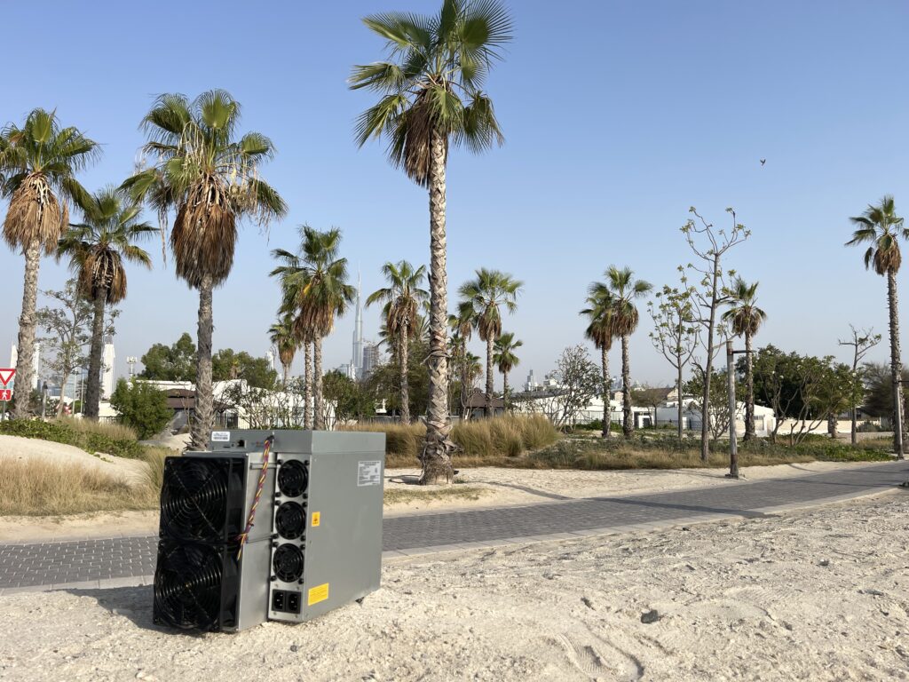 Antminer S19 Pro in the sand of Dubai with Palm trees
